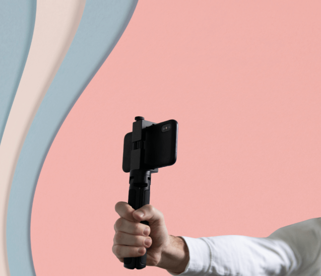 An outreached arm holding a smartphone. The background is pink, blue, and white.