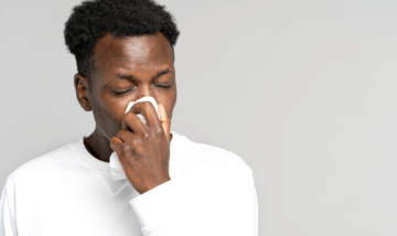 Young black man wearing a white shirt blowing his nose into a tissue